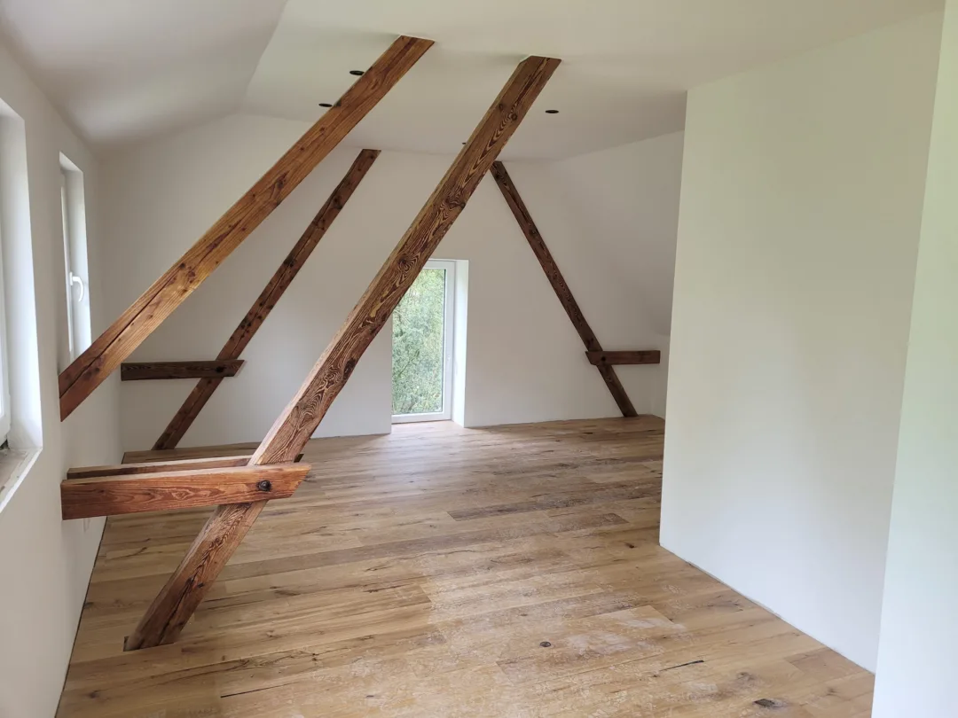 Ausgebautes Dachzimmer mit erhaltenen alten Balken und Kopfbändern, weiße Wände, Eichenboden