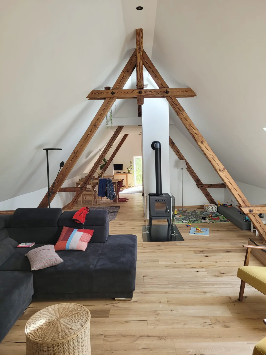 Offener Wohnraum unter dem sichtbaren alten Dachstuhl, in der Mitte ein Kaminofen