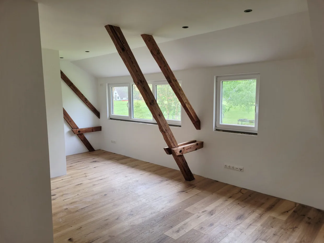 Helles Dachzimmer, alte schräge Streben vor weißer Wand, Fenster zum Garten