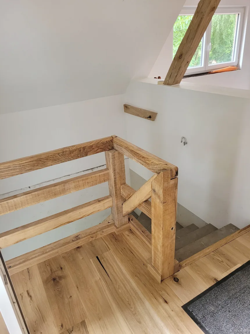 Treppenöffnung mit Geländer aus altem Holz, darüber ein Fenster in der Schräge